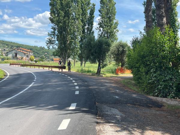 Der Trasimeno-Radweg am Ortsausgang von San Feliciano. Eine asphaltierte Straße macht eine Kurve nach links. Auf der rechten Seite ist ein Radweg.